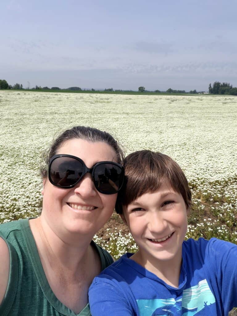 Jenn and son smiling in front of a field of white flowers.