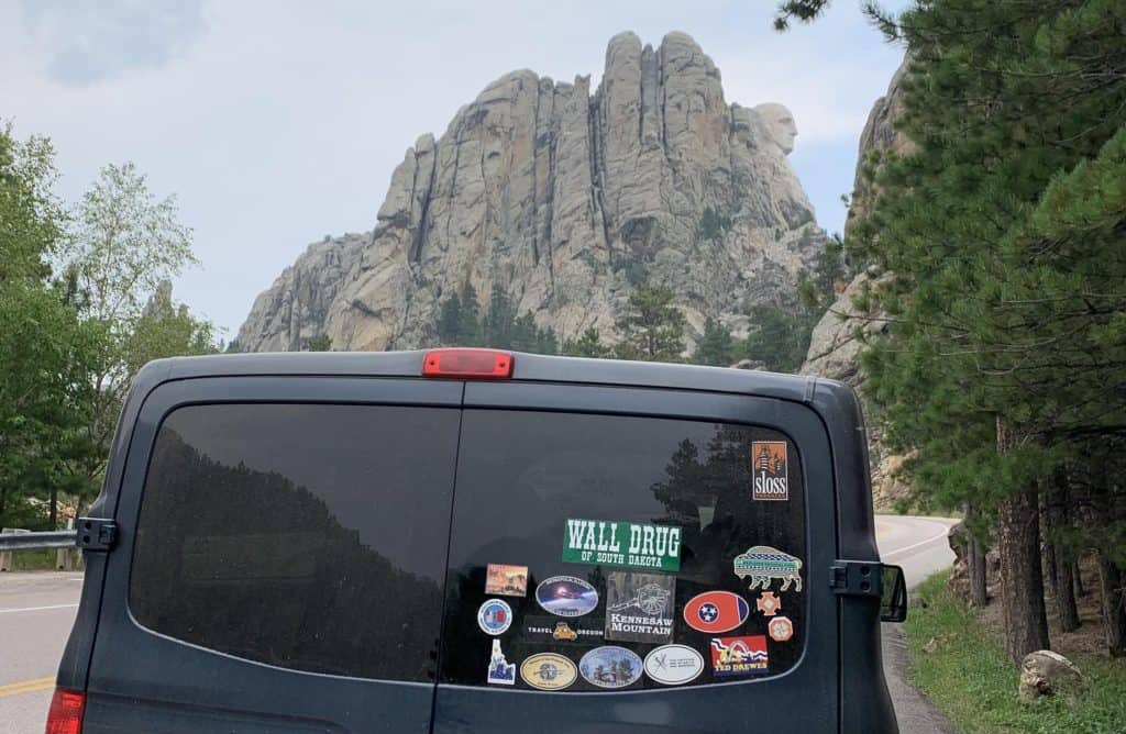 rear of van with bumper stickers in front of Mount Rushmore. Road Trips can provide a great reset from normal life.