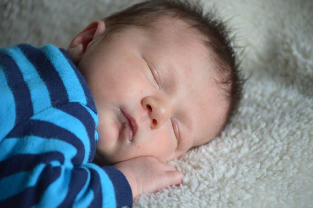 Sleeping newborn infant in blue striped shirt. Best baby registry ideas.