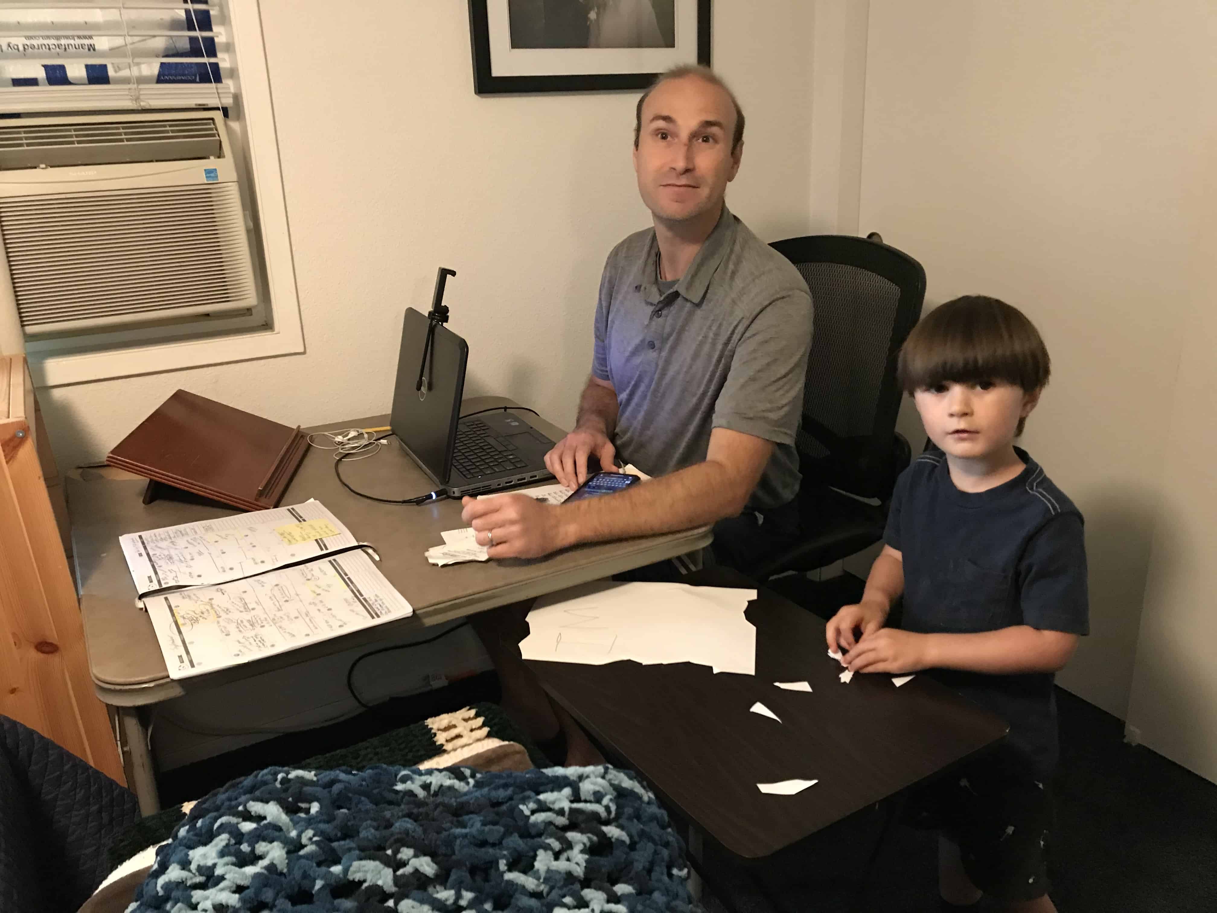 man working at table with child playing next to him