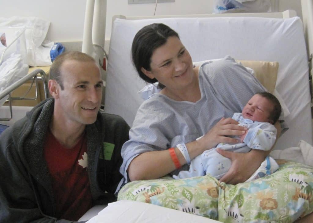Mother, father and newborn in a hospital bed.