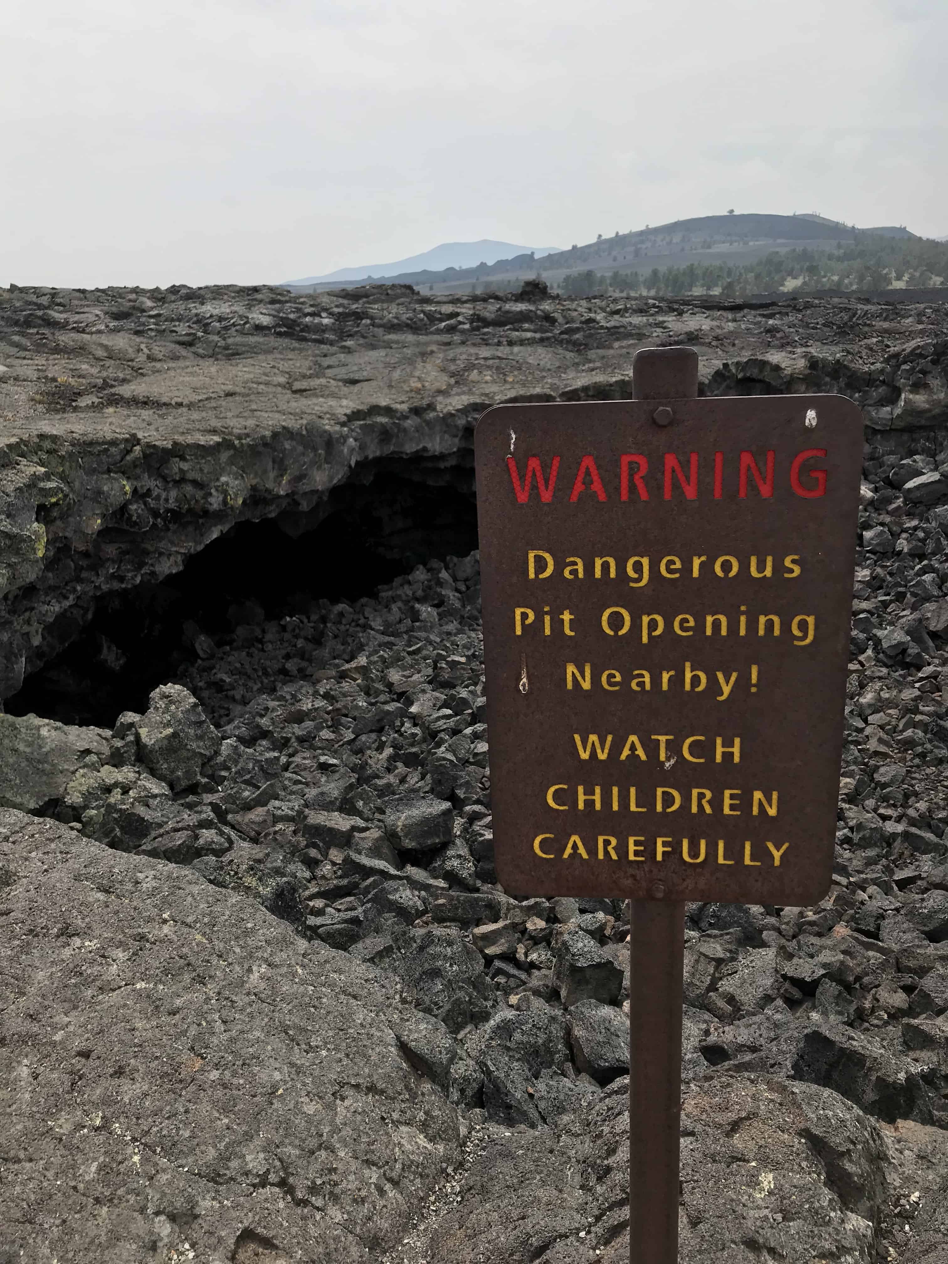 Sign in front of lava tube entrance says: "Warning Dangerous Pit openings nearby! Watch Children Carefully." Craters of the moon Idaho with kids