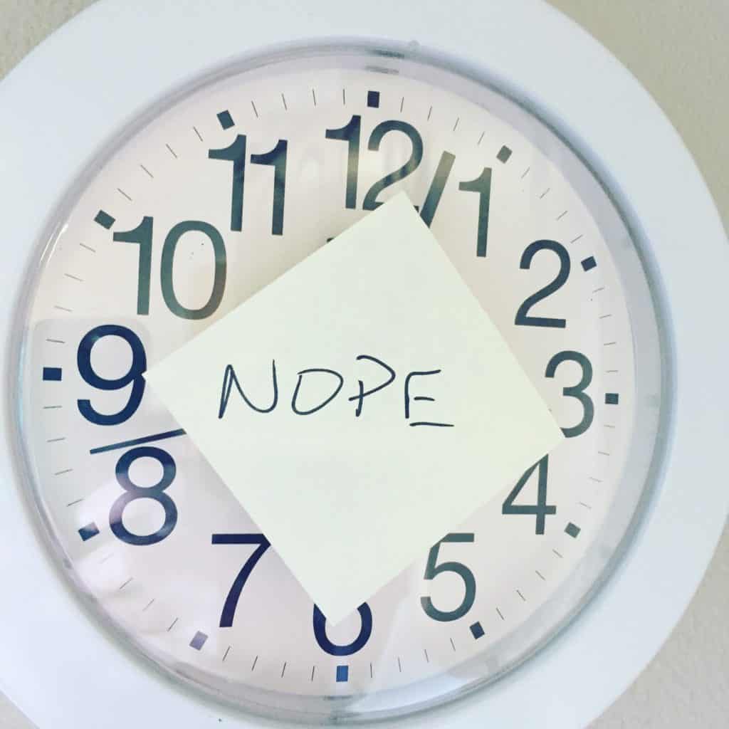 white clock face with sticky note over hands with text that says nope