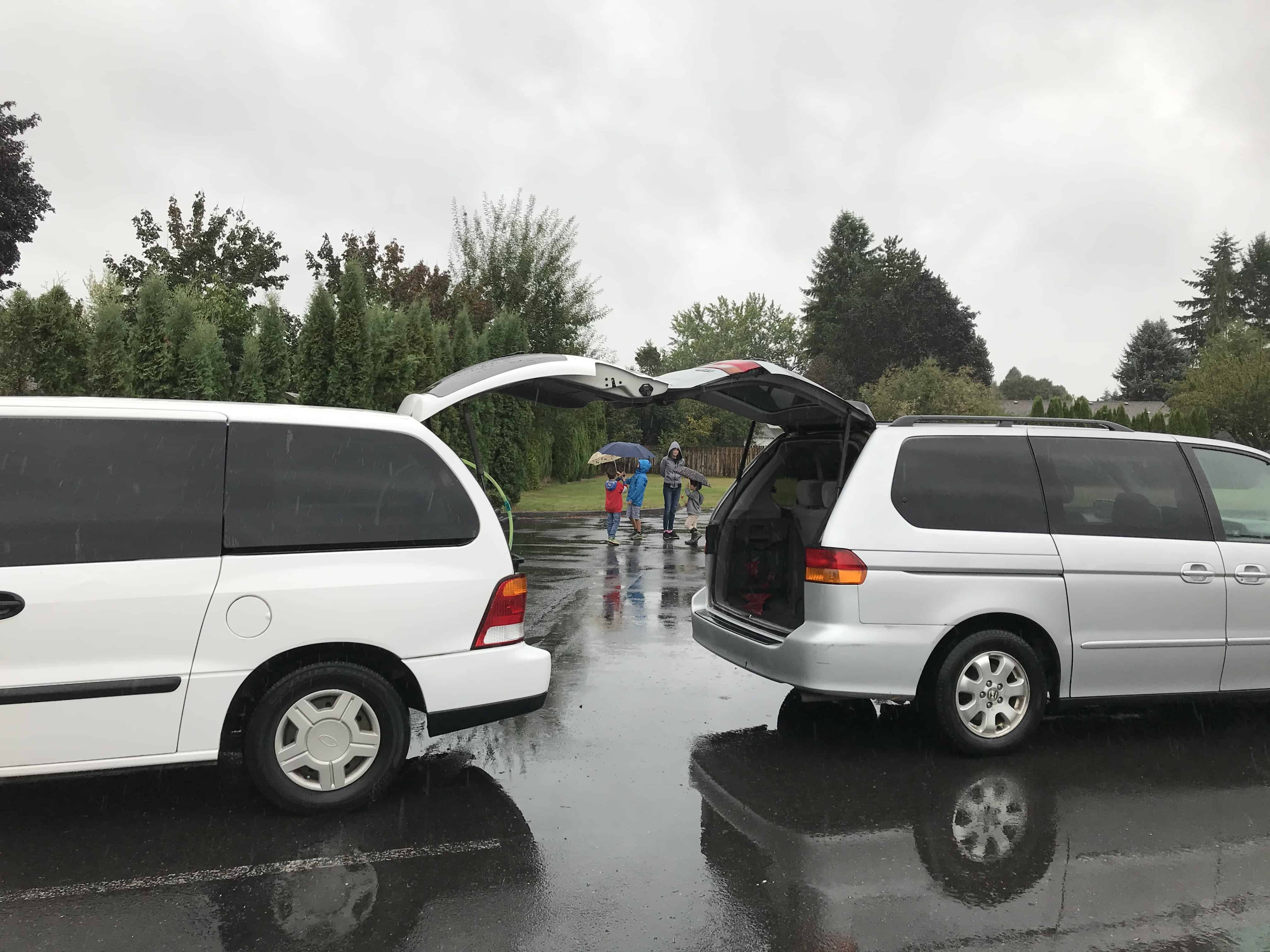 white minivan with rear door open facing away from gray minivan with rear door open. Our Nissan NV 3500 is much better than both!