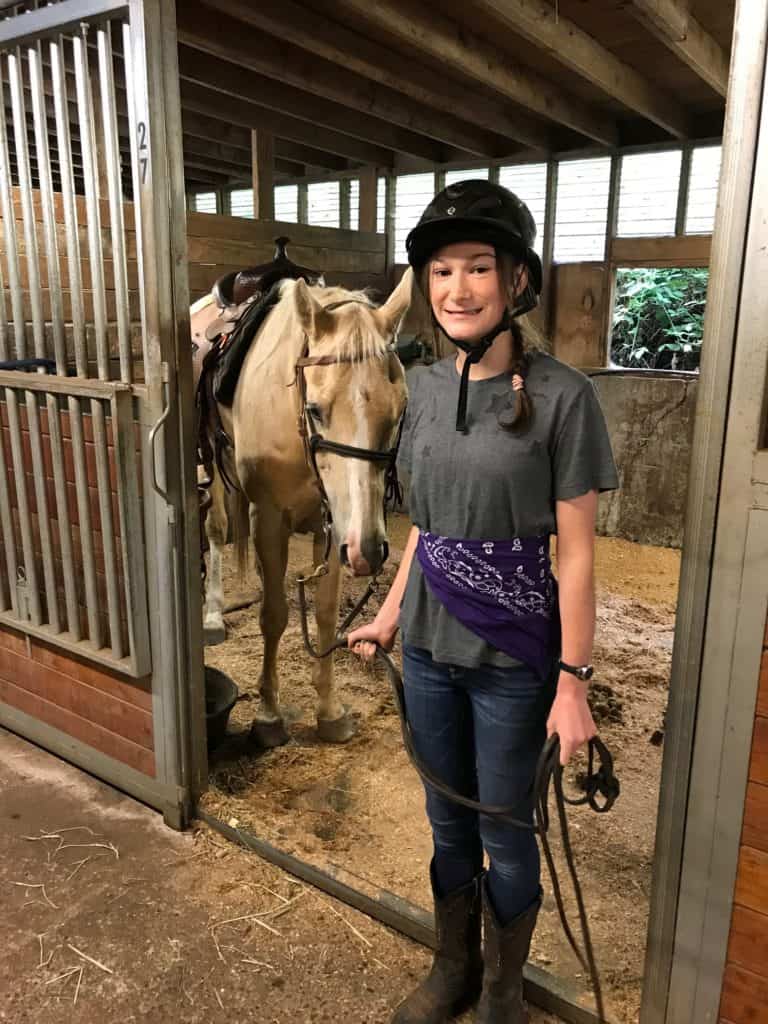 teen girl with helmet in stable with palomino horse on lead line