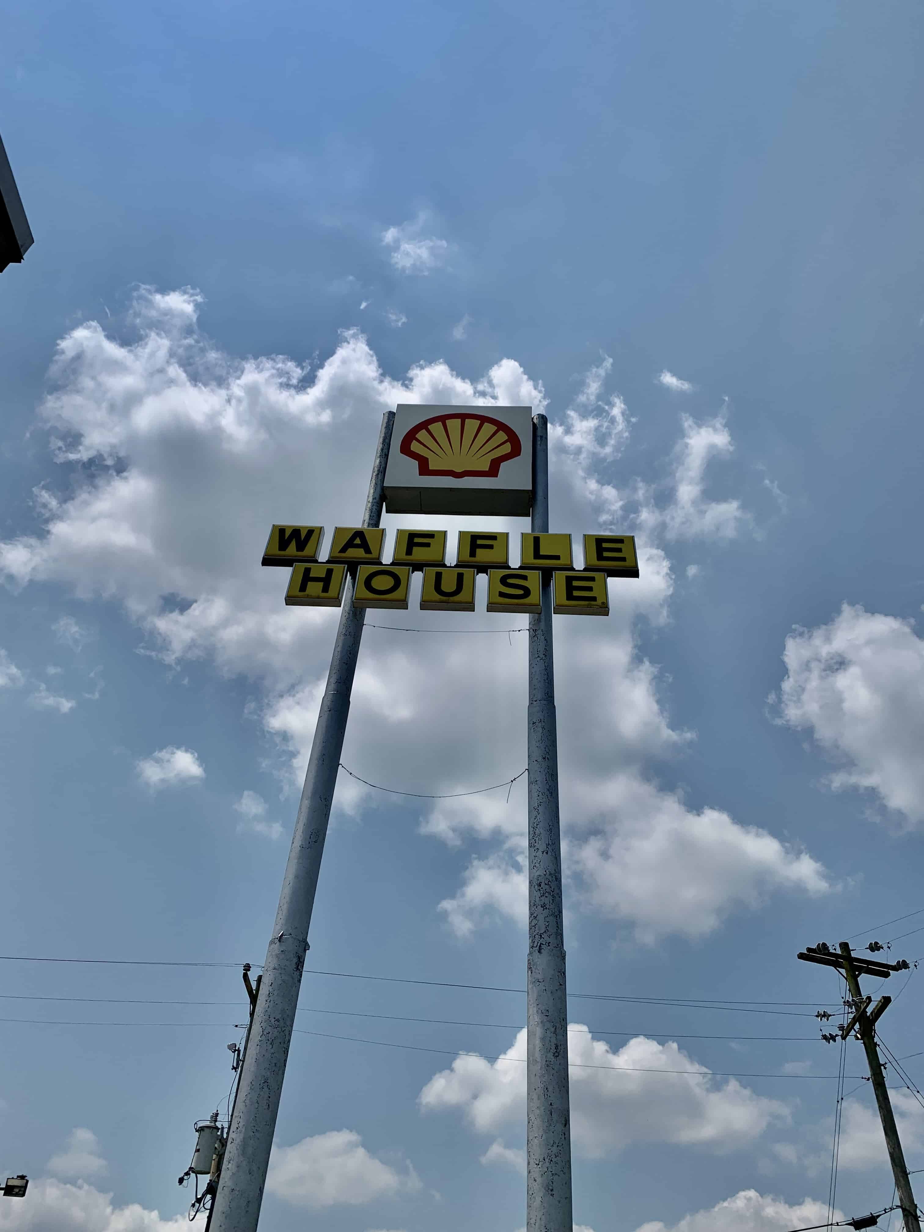Shell gasoline sign with Waffle House sign below, blue sky background