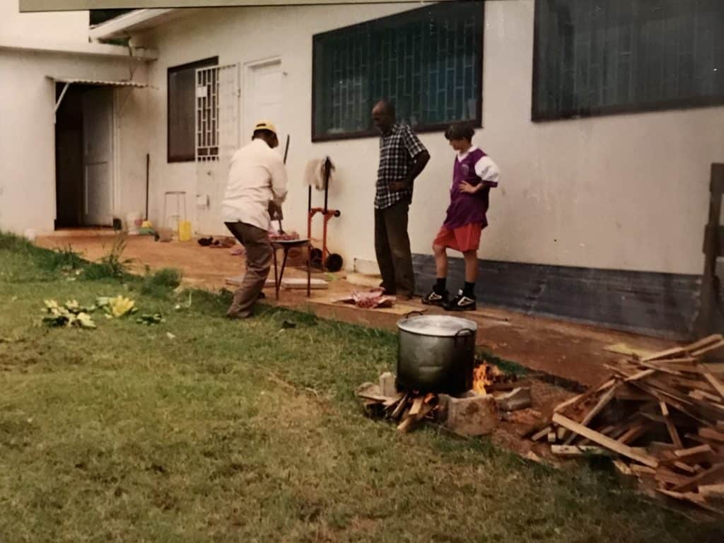 boy and two men with cooking pot in foreground