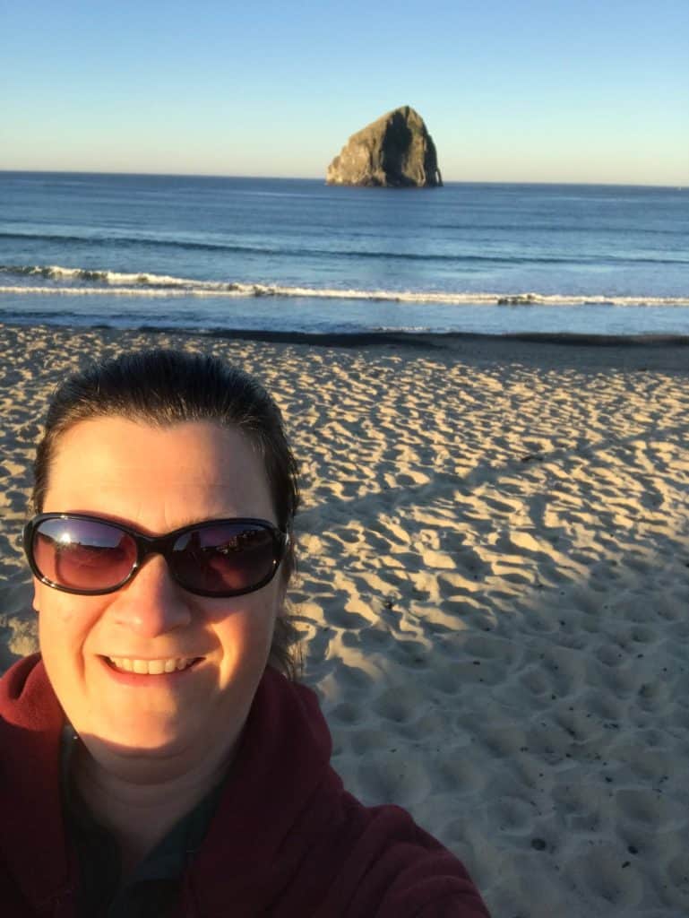 woman in hoodie and sunglasses in front of haystack rock at Pacific City. 