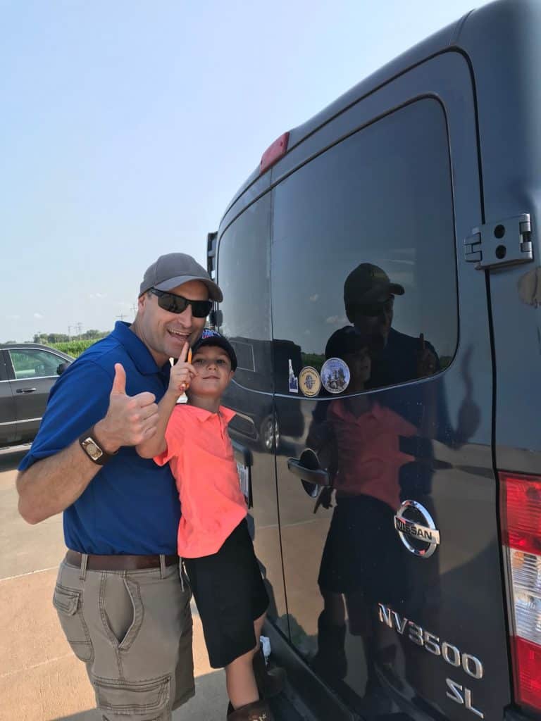 Man and boy adding a bumper sticker to the Nissan NV 3500. Three bumper stickers and counting! This road trip is heating up!