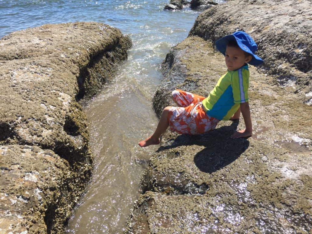 boy dipping foot in sea water near tide pool