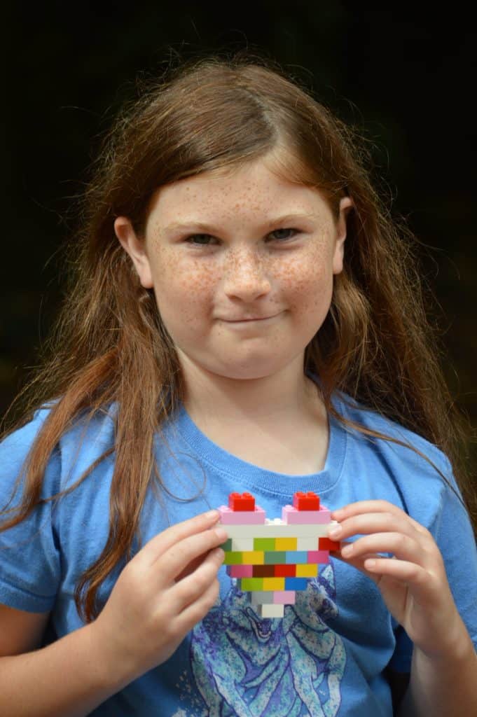 Girl holding LEGO heart. Doing LEGO challenges, like building a heart, is one of the easy activities to do with kids.