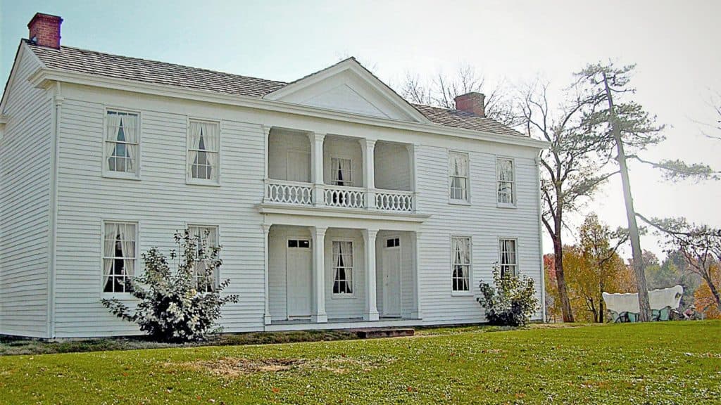 The Alexander Majors house stands majestically. The house is a white, two-story mansion. A covered wagon stands nearby.