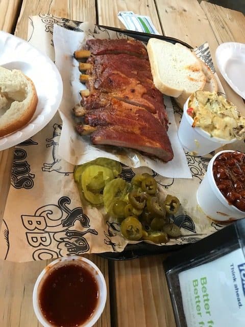 Meal at Slap's BBQ including ribs, baked potato casserole, baked beans, bread, condiments and BBQ sauce.