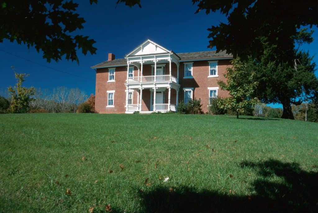 The Grinter home stands on top of a green hill surrounded by trees. The house is a two-story brick mansion with white trim.