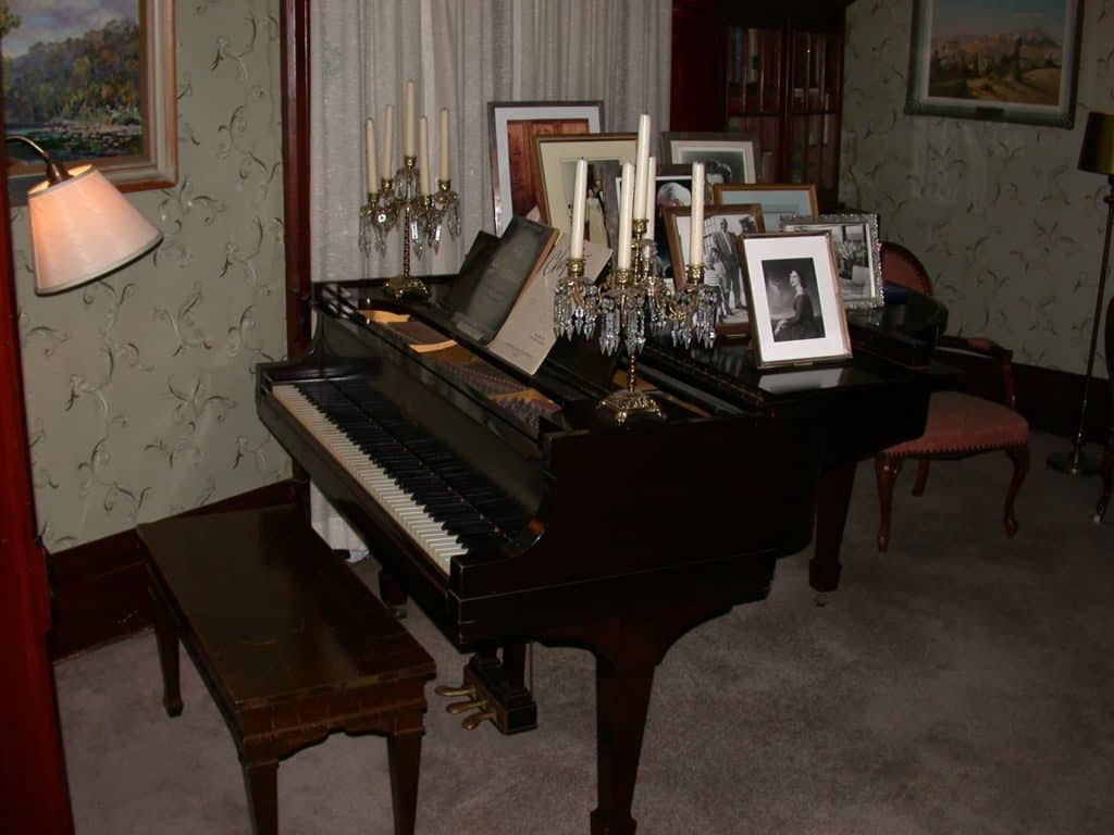 Two ornate candelabras and eight photo frames clutter the top of a beautiful baby-grand piano.