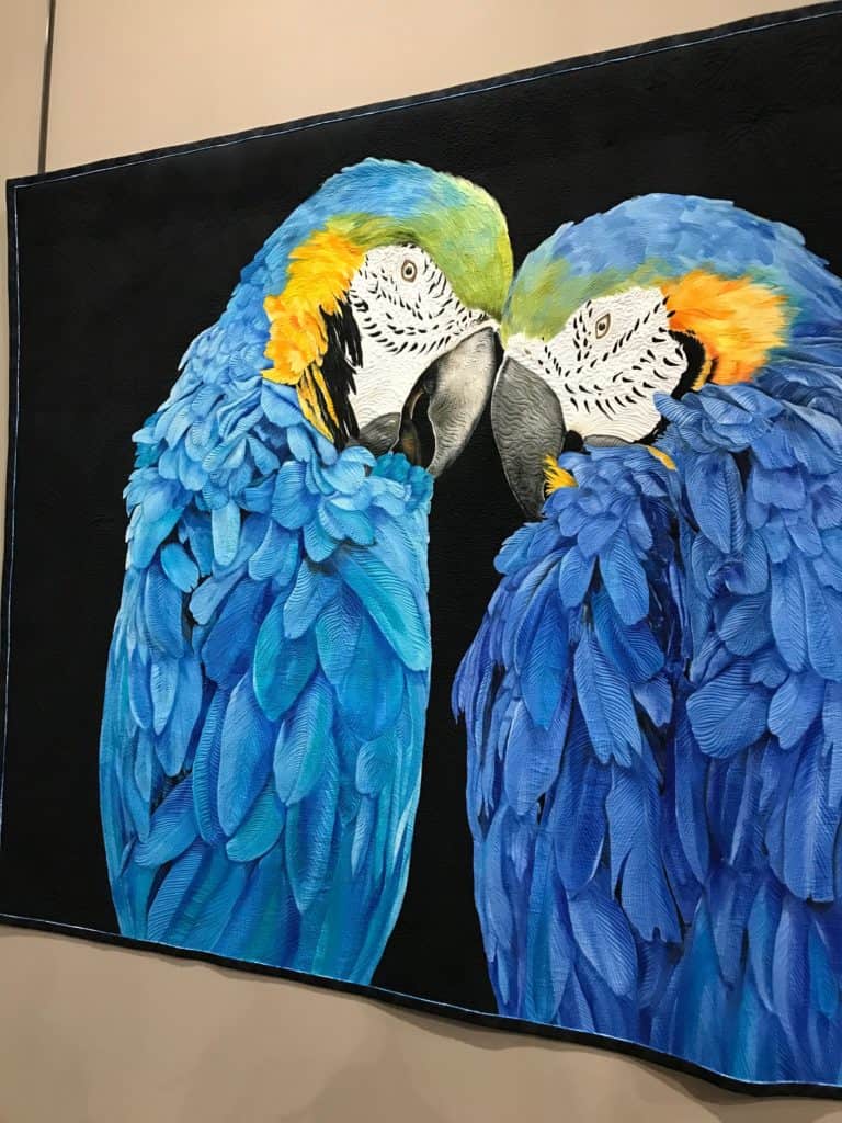 Quilt showing 2 blue macaw parrots on a black background at the National Quilt Museum in Kentucky.