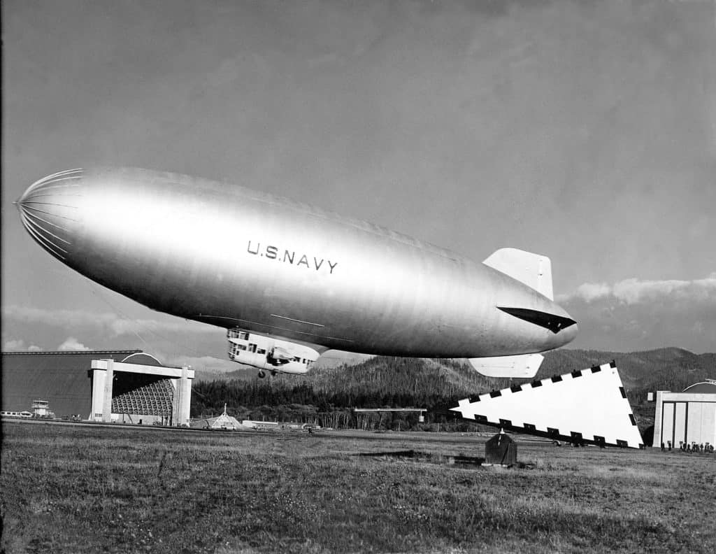 The black and white photo shows a K-Class blimp hovering over a field at NAS Tillamook. The unique history of NAS Tillamook is one reason to visit the Tillamook Air Museum.