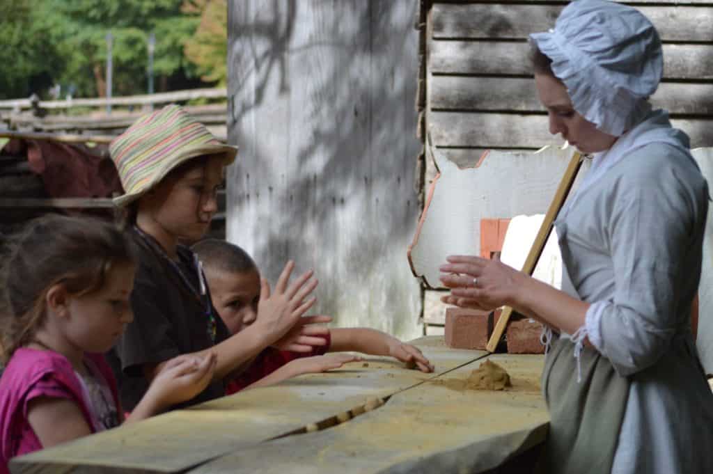 Children learning from woman in historical dress.