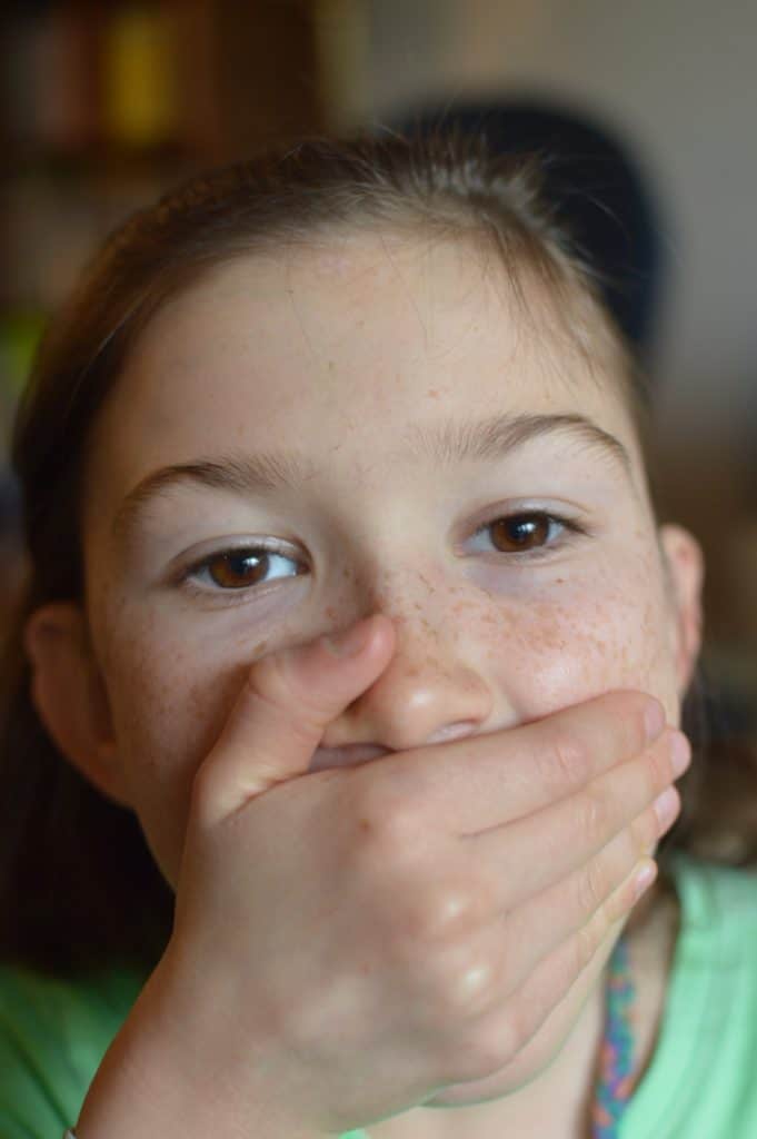 Girl covering mouth with hand. Blurting out responses is typical with hyperactive ADHD type.