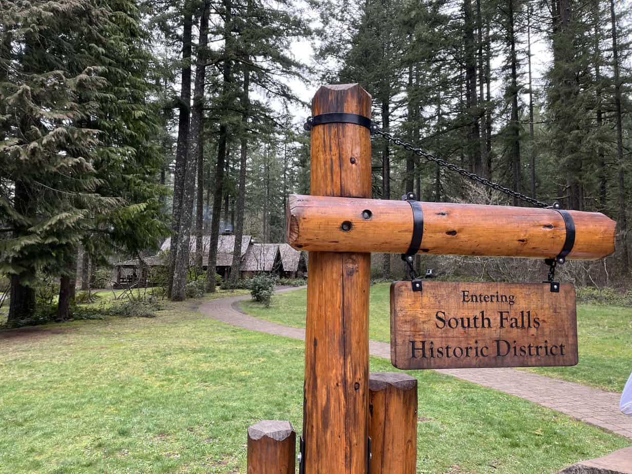 A rustic sign welcomes visitors to the South Falls Historic District. The historic South Falls Lodge stands in the background.