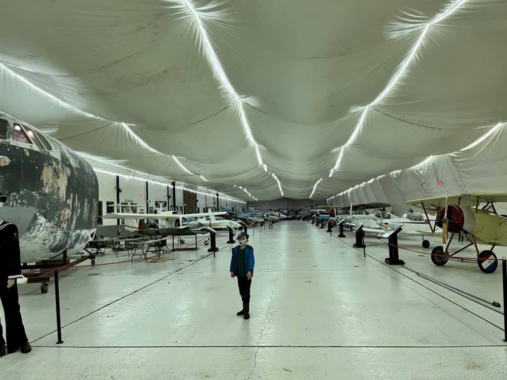 Boy inside tented area of Hangar B, with dozens of small aircraft on either side.