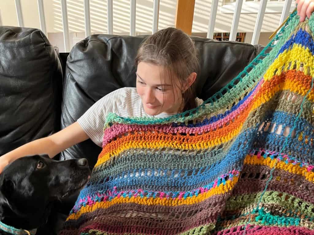 Girl crocheting a blanket with dog. ADHD in teen girls can look like constant activity with hands or feet.