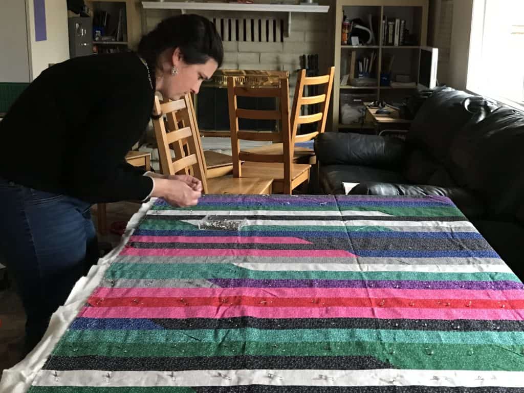 Woman pinning a quilt top on a table. Hobbies are great self-care ideas for anxiety.