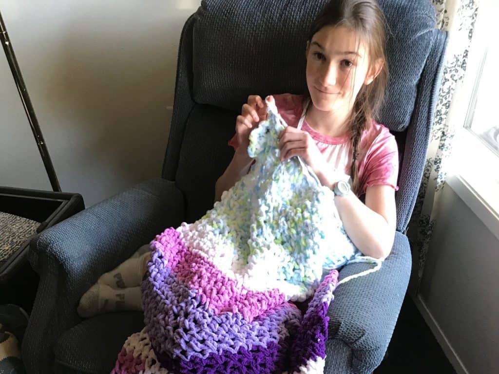 Girl finger crocheting a blanket.