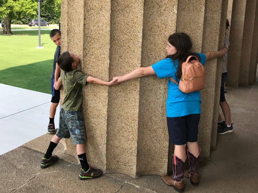 Kids holding hands around a column at the Nashville Parthenon. 