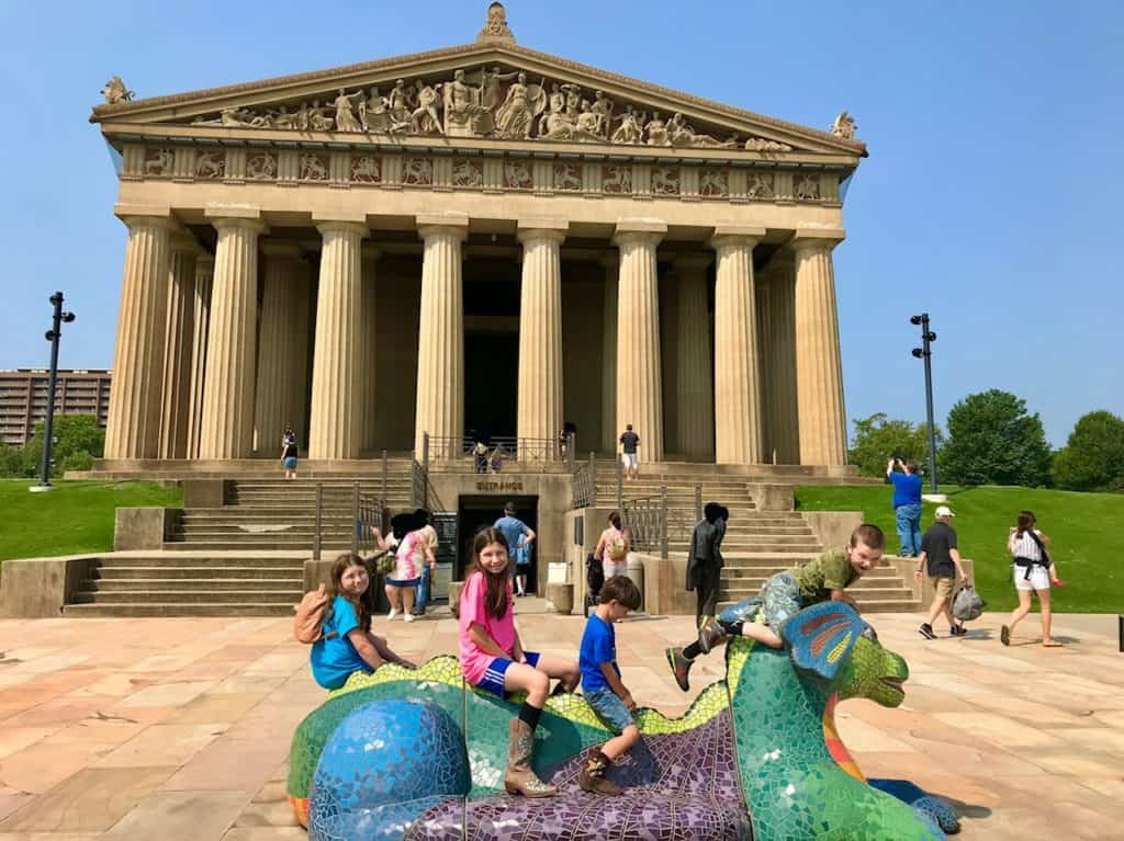 Entrance to the Nashville Parthenon, with kids sitting on dragon statue in foreground.