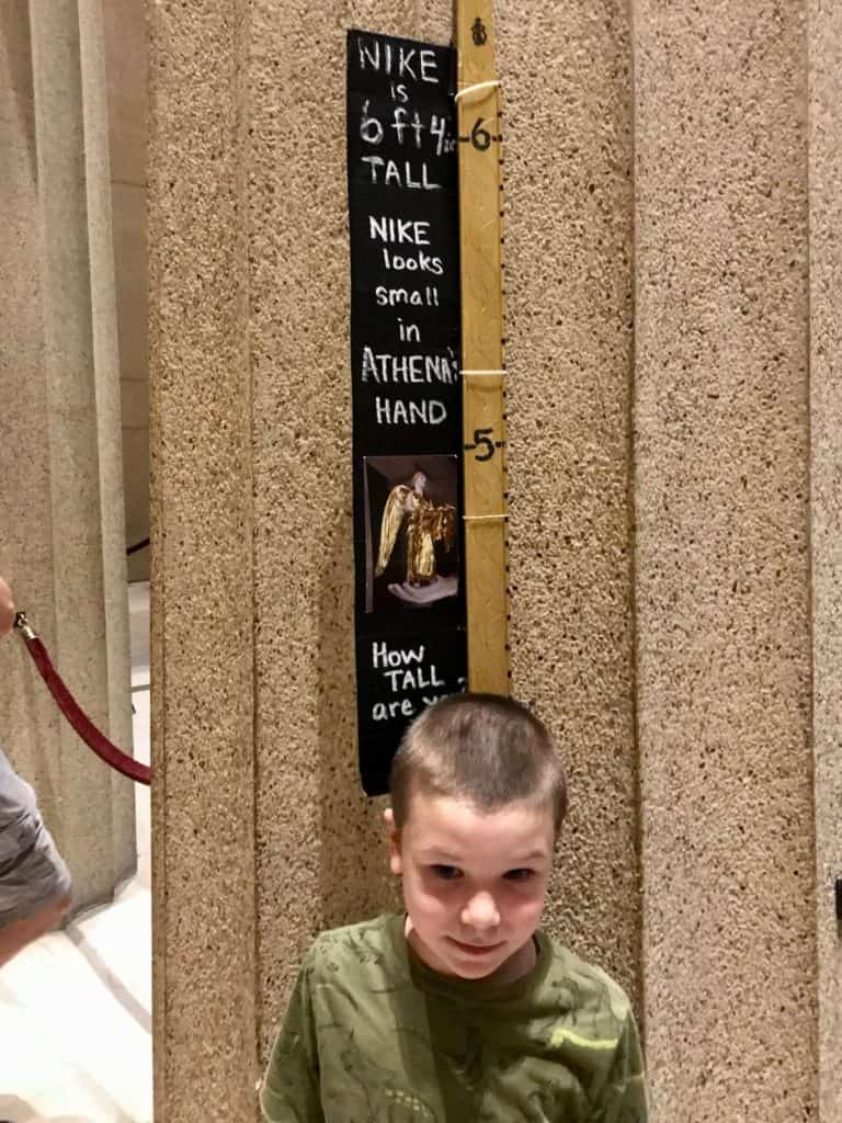 Boy in front of measuring stick to see how his height compares with the Nike statue.