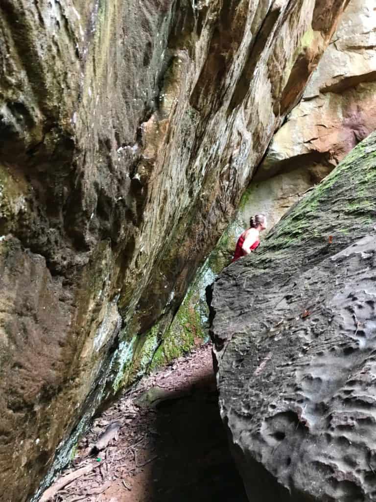Woman climbing through space between boulders at Moss Rock Preserve.