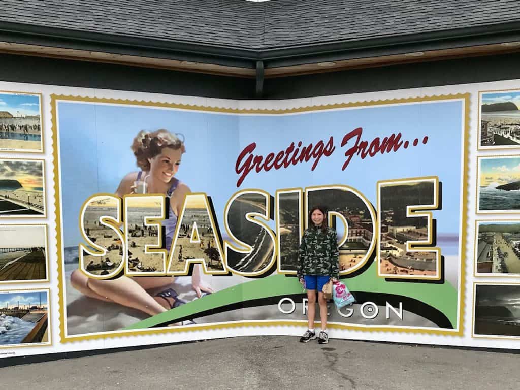 Seaside postcard mural with girl in front. Visiting Seaside Oregon with kids is a great plan for a family vacation.