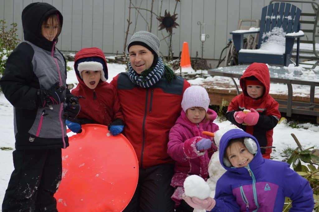 Man and 5 children in snow gear playing in the snow. Who to talk to about ADHD.