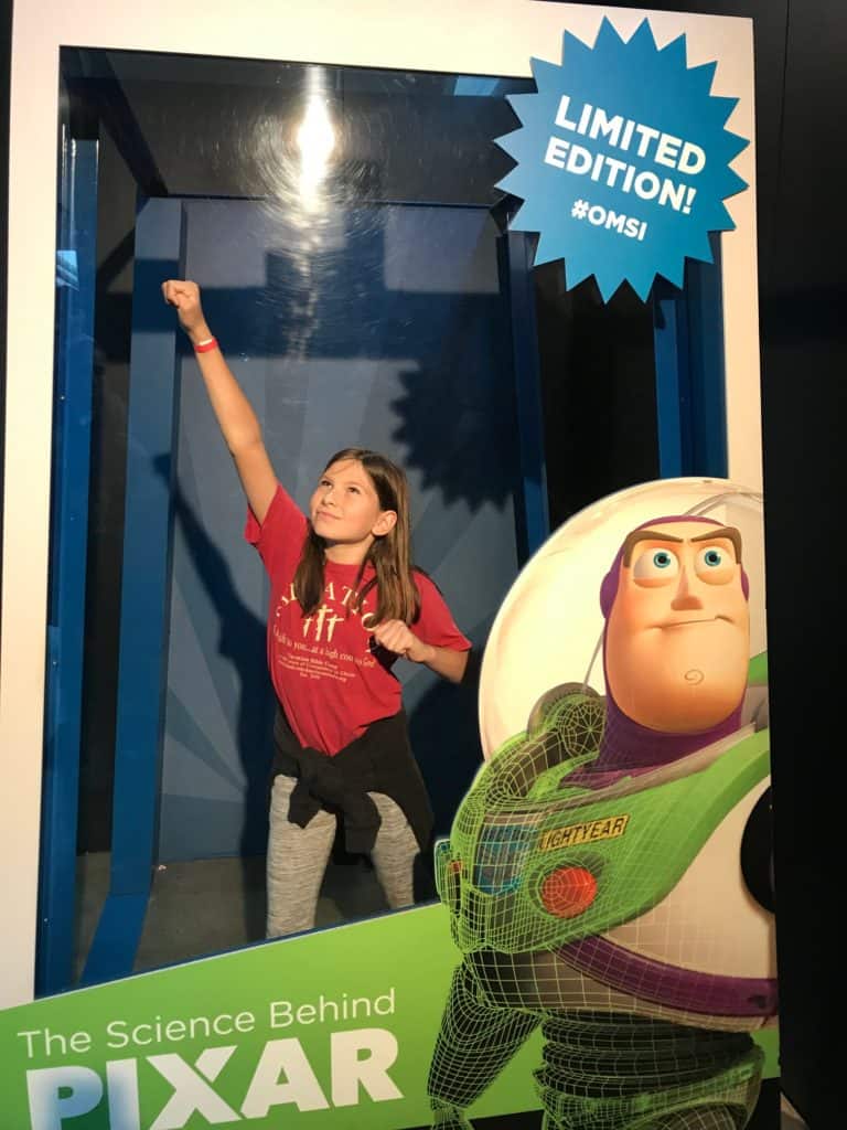 Girl in superhero pose with Buzz Lightyear cutout.