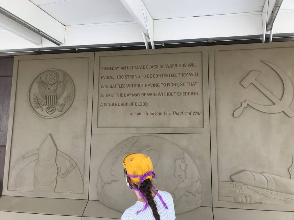 Girl looking at engraving inscribed with Cold War imagery and a Sun Tzu quote from the Art of War. Missile Silo National Park.