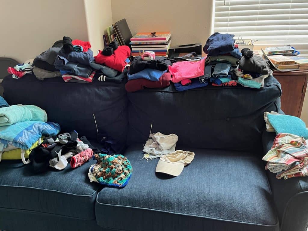 Folded stacks of clothing on a couch. Kids clothing organization tips.