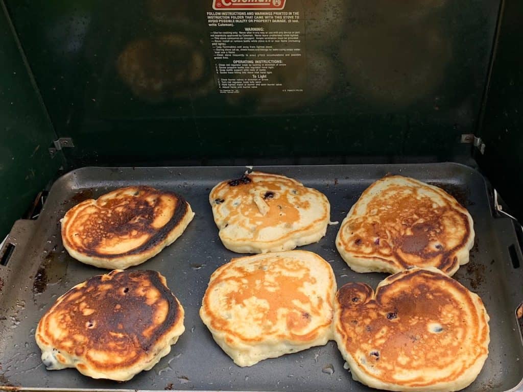 Pancakes cooking on a camp stove griddle. Easy camping meal ideas and no cook camping meals.