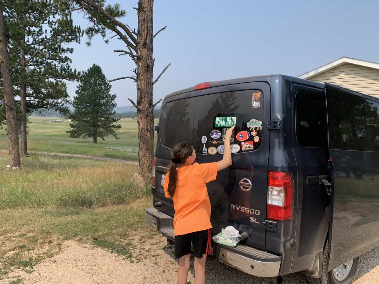 Girl applying bumper sticker to back window of van.