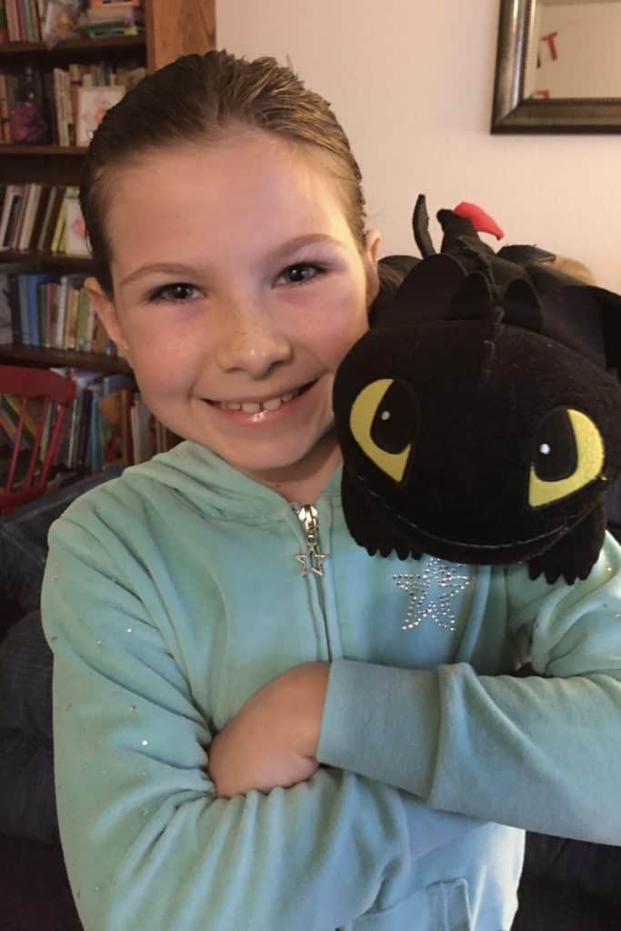Girl with stuffed Toothless character dragon on her shoulder.