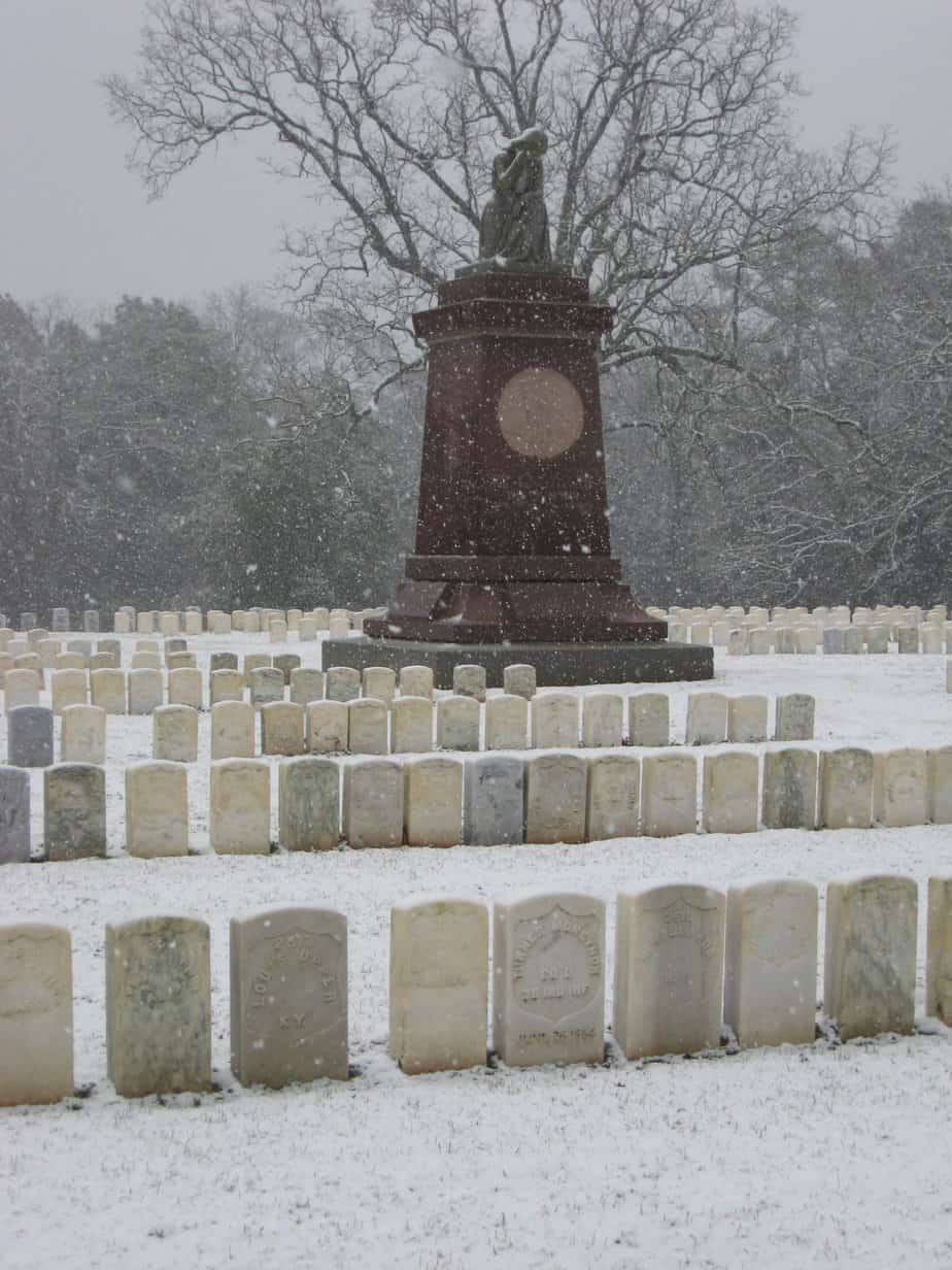 snow collects on top of a stone woman who weeps over her dead. The monument stand above rows of tightly packed military gravestones.