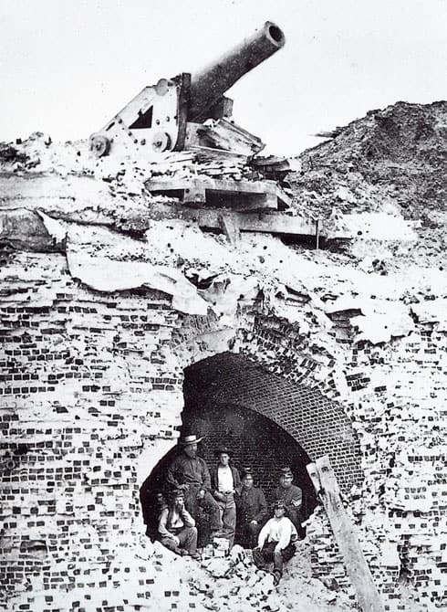 A black and white picture shows soldiers standing in a gaping hole that was blown open in the wall of Fort Pulaski.