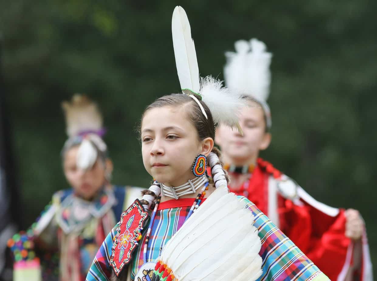 A Native American girl stands proudly adorned in the traditional clothing of her people.