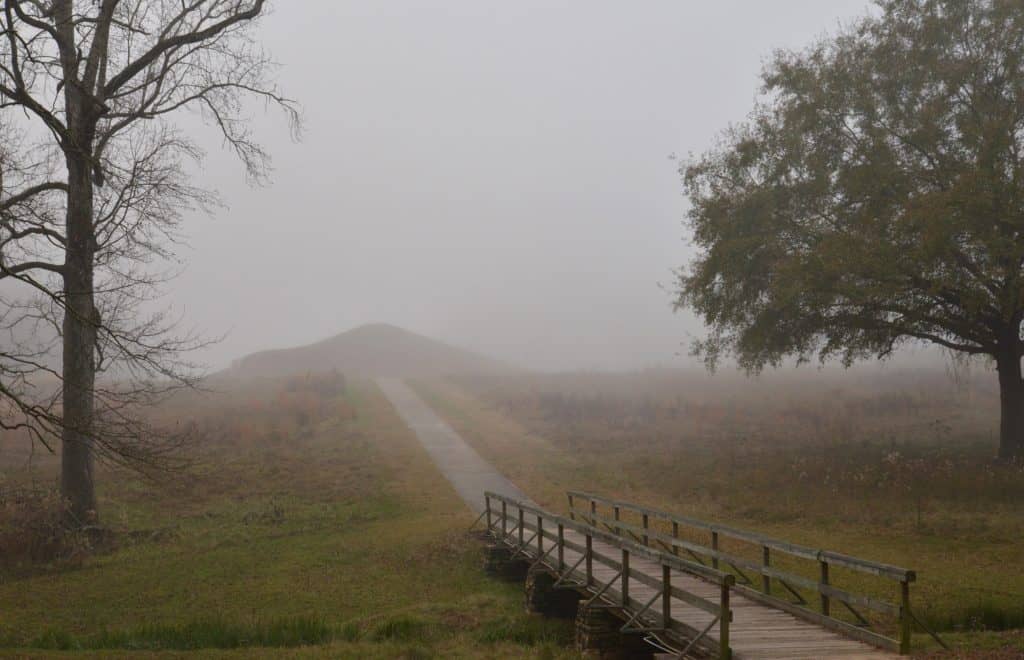 A bridge and pathway lead to an ancient ceremonial mound.