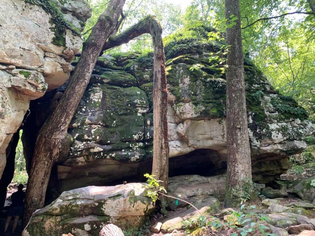 A woman walks through an tall, narrow cleft between two gargantuan boulders at Moss Rock Preserve.