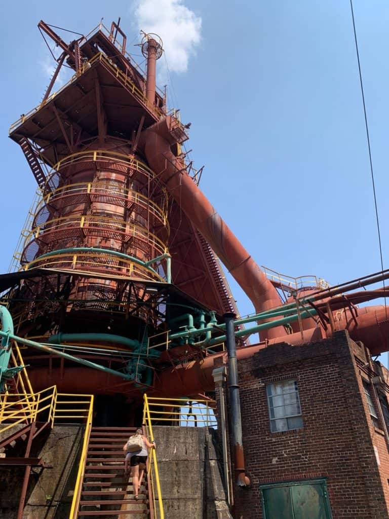 A woman walks up a stairway that leads up to an enormous furnace. Educational value makes the Sloss Furnaces one of the 17 best hiking trails Birmingham AL.