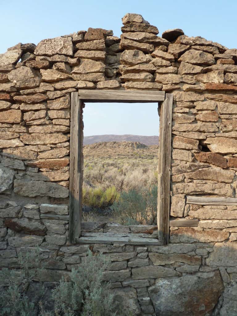 The window of an abandoned, stone house frames a scene of desert scrubland in Eastern Oregon. Eastern Oregon is one of the 15 best Portland Oregon day trips for families.