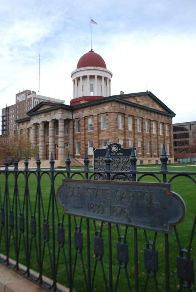 Springfields Old State Capitol building stands behind an iron fence that say "Old State Capitol 1839-1876."