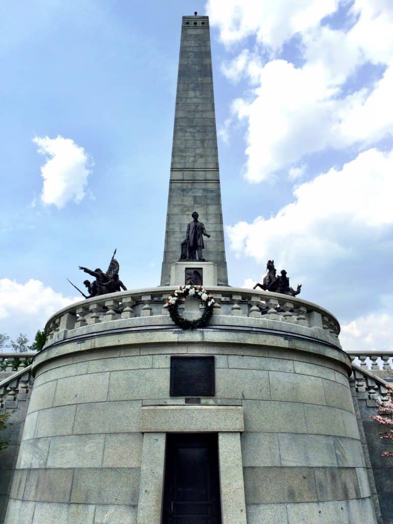 A bronze statue of Lincoln stands framed by his monumental tomb.