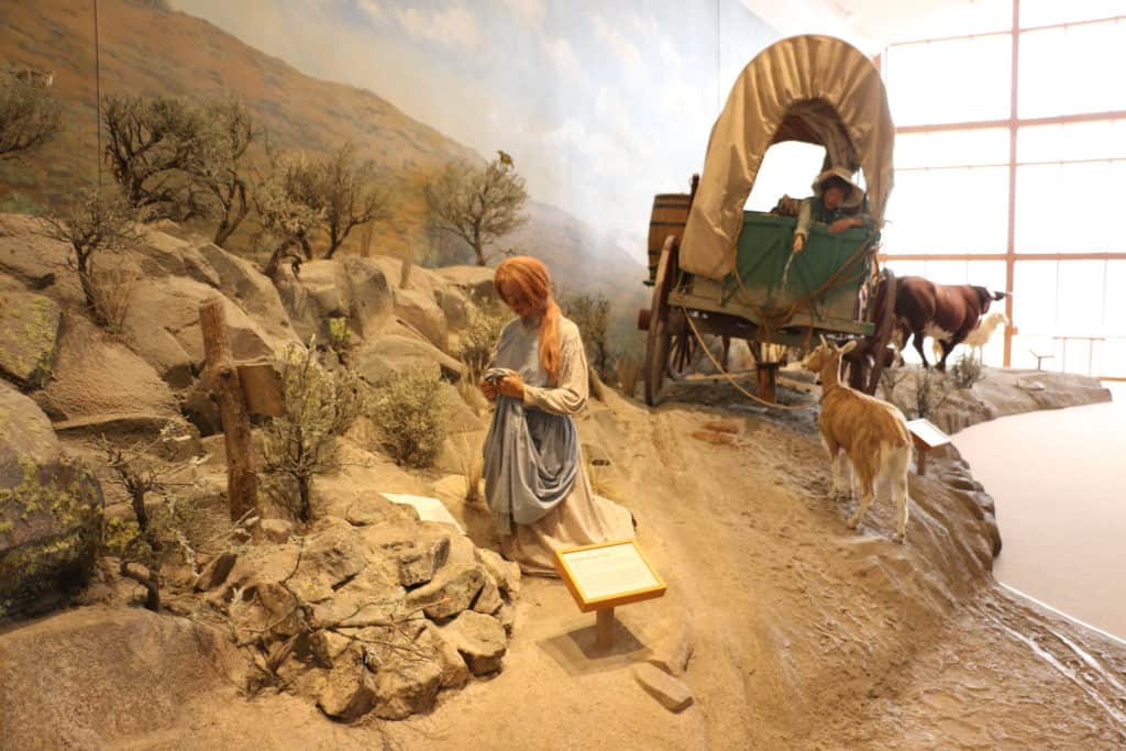 A woman kneels beside a grave in a display at National Historic Oregon Trail Interpretive Center.